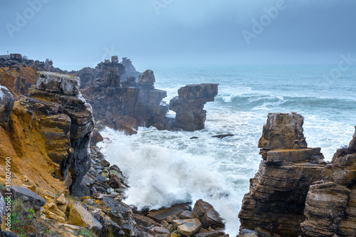 A huge ocean waves breaking on the coastal cliffs in at the cloudy stormy day. Breathtaking romantic seascape of ocean coastline. Peniche  Portugal.