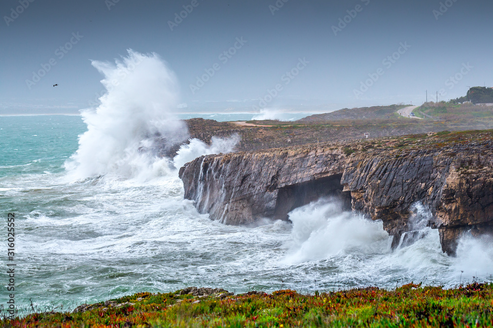 A huge ocean waves breaking on the coastal cliffs in at the cloudy stormy day. Breathtaking romantic seascape of ocean coastline. A huge ocean waves breaking on the coastal cliffs in at the cloudy stormy day. Breathtaking romantic seascape of ocean coastline.