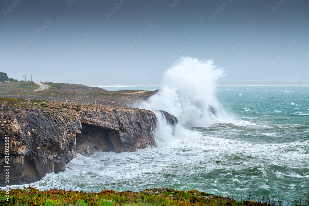 A huge ocean waves breaking on the coastal cliffs in at the cloudy stormy day. Breathtaking romantic seascape of ocean coastline. Peniche, Portugal.