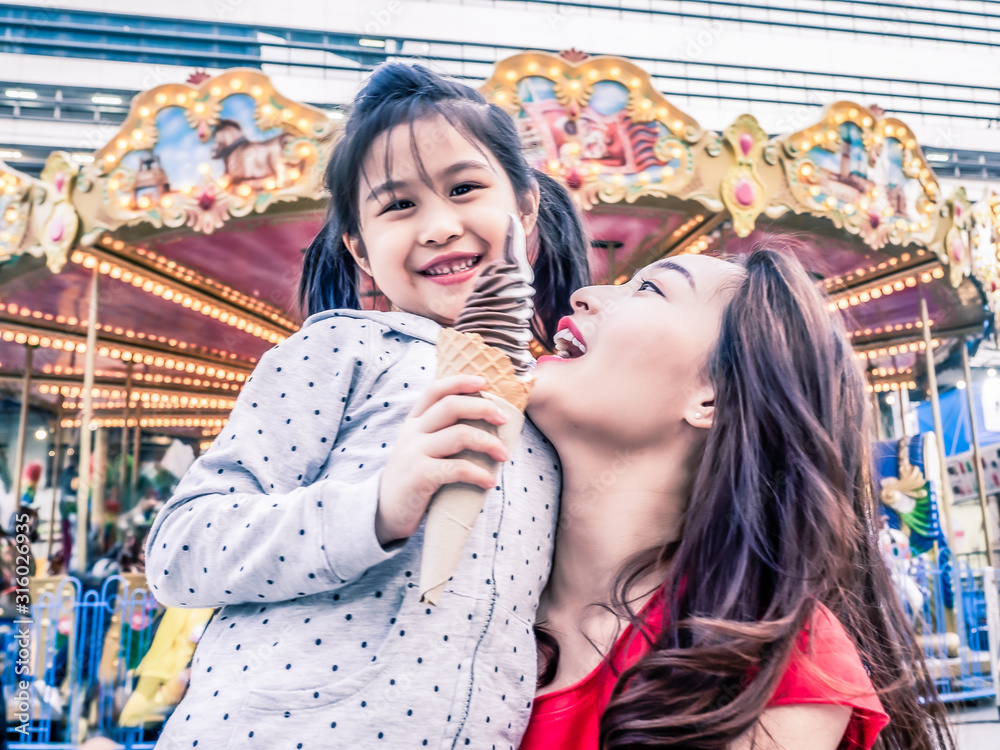 happy asia mother and daughter have fun in amusement carnival park with farris wheel and carousel background