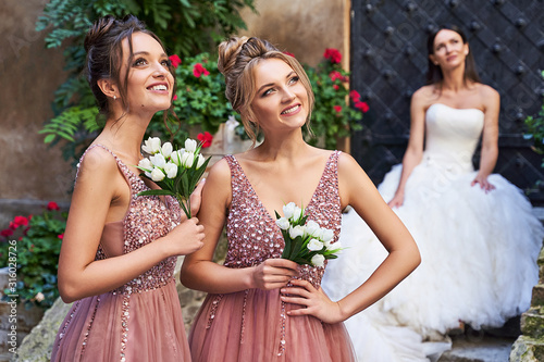 Obraz na płótnie Beautiful bride and bridesmaids in gorgeous elegant stylish red pink violet floor length v neck chiffon gown dress decorated with sequins sparkles and rhinestones holding flowers bouquets. Wedding day w salonie