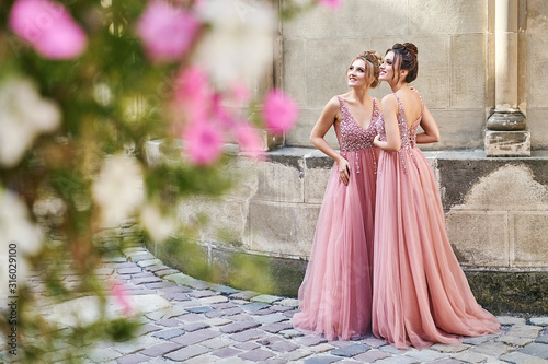 Beautiful bridesmaids in gorgeous elegant stylish red pink violet floor length v neck chiffon gown dress decorated with sequins sparkles and rhinestones holding flowers bouquets. Wedding day in old