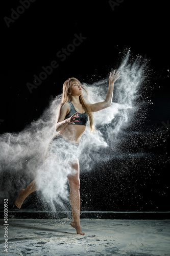 Beautiful girl model on a black background throws flour