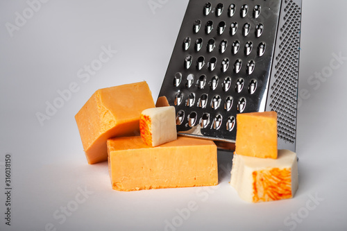 Close up of hand held cheese grater blocks of sharp cheddar  and white cheese on solid background photo