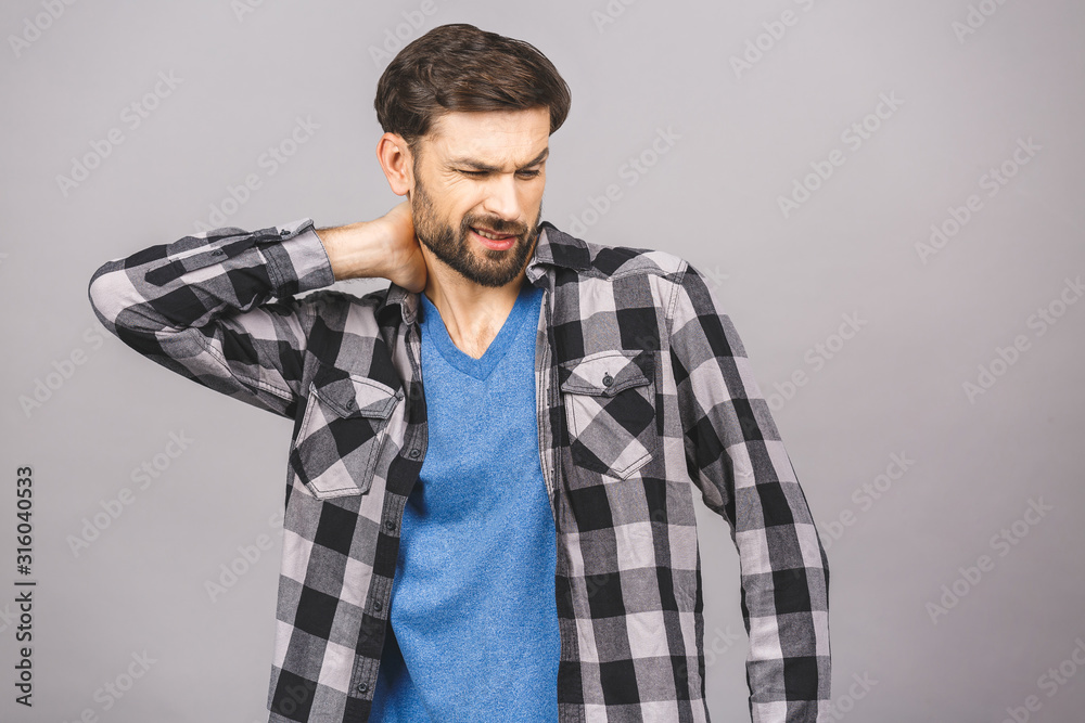 Feeling pain in neck. Frustrated young man incasual touching his neck and expressing negativity while standing against grey background. Feeling pain in neck. Frustrated young man incasual touching his neck and expressing negativity while standing against grey background.