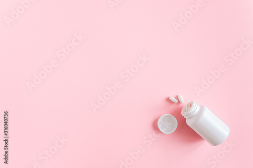 White medical bottle and two pills dietary supplements, nutraceuticals, antibiotic, painkillers on pink background. Health and drug treatment concept. Top View Copy Space.