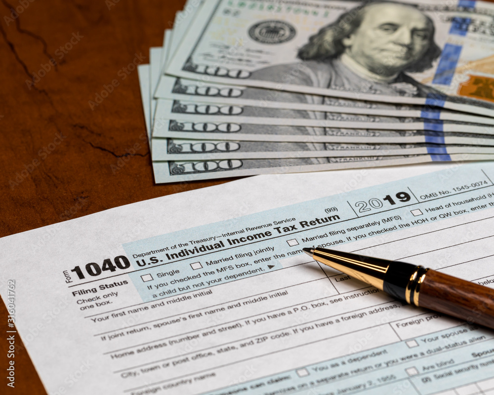 Obraz premium 1040 individual income tax return form 2019 with ballpoint pen 100 dollar bills. Concept of filing taxes, payment, refund, and April 15, 2020 deadline date