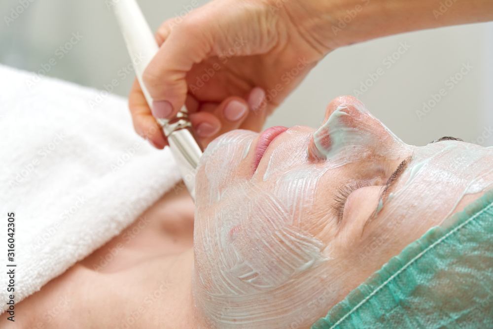 Beautician applies a natural moisturizing mask to the face of a young beautiful woman. Anti-aging and wrinkle mask is applied to the face with a brush. Cosmetology concept. The cosmetologist performs Beautician applies a natural moisturizing mask to the face of a young beautiful woman. Anti-aging and wrinkle mask is applied to the face with a brush. Cosmetology concept. The cosmetologist performs