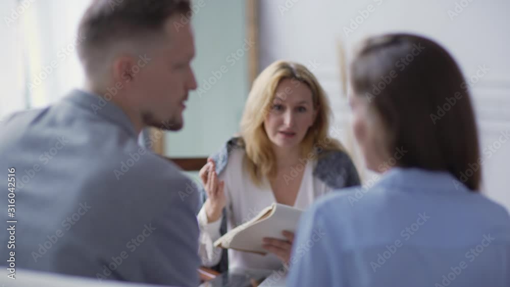 Rack focus of female therapist with notepad trying to explain solution of relationship problem to young couple arguing during therapy session Rack focus of female therapist with notepad trying to explain solution of relationship problem to young couple arguing during therapy session