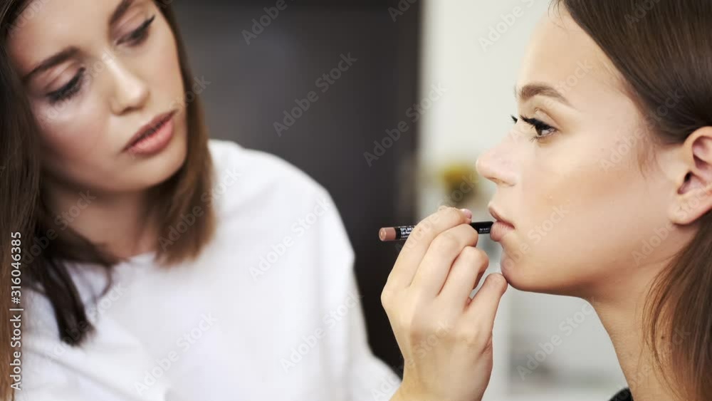An artist is doing a makeup. A client is a brunette woman. The girls are in a salon. An artist is doing a makeup. A client is a brunette woman. The girls are in a salon.