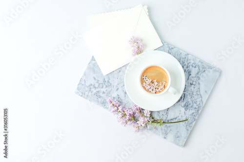 Minimal elegant composition with coffee cup and lilac branches, envelope on white background, female morning breakfast, woman mother day, saint valentine day, wedding