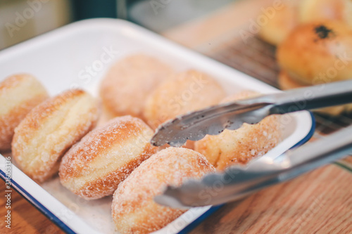 Closeup of woman holding clamp picking sugar-glazed doughnuts a bakery store.taking fresly baked bun from the display for a customer. photo