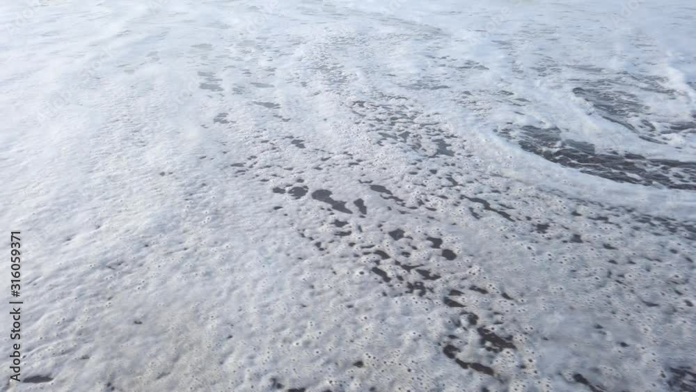Close up of calm ocean waves foam slowly covering sand on beach during bright sunset at Tenerife, Canary Close up of calm ocean waves foam slowly covering sand on beach during bright sunset at Tenerife, Canary