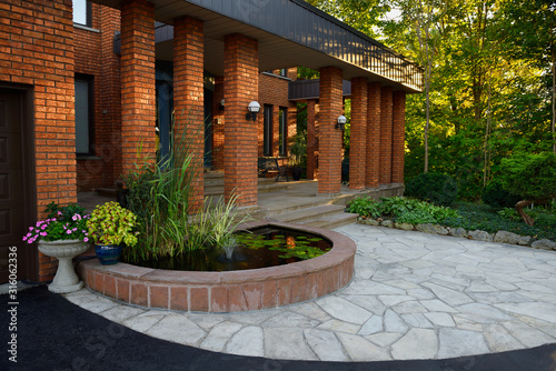 Front entrance with pond and stone veranda on red brick house with pillars © Reimar
