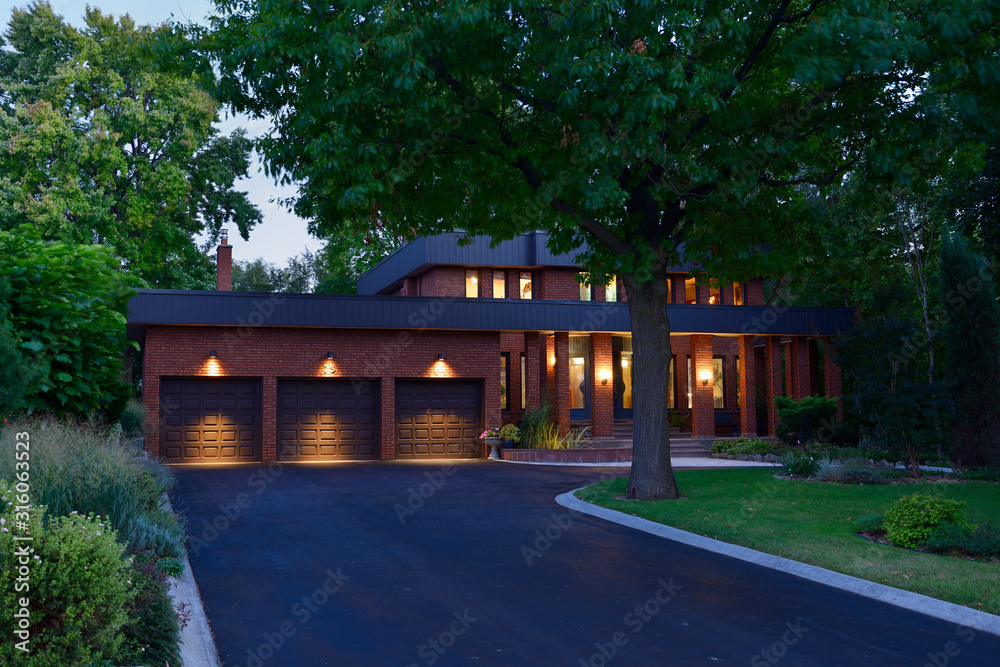 Red brick house with circular driveway and triple garage at dusk Stock