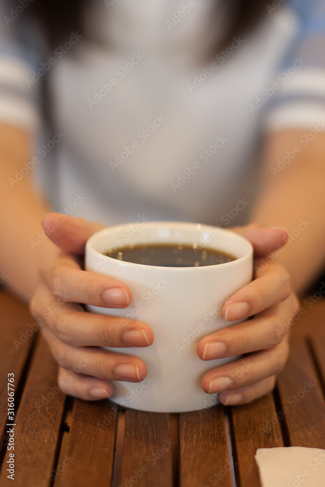 closeup woman hand holding a white cup of hot americano coffee on the table closeup woman hand holding a white cup of hot americano coffee on the table