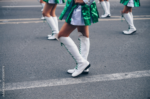 Low section of majorette in white and green silk uniform feet marching on the road pavement. Selective focus. Copy Space. Closeup.
