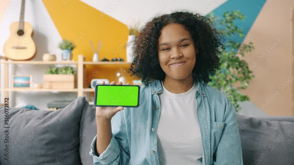 Portrait of happy Afro-American lady holding copy space green screen smartphone at home smiling looking at camera. Technology and lifestyle concept. Portrait of happy Afro-American lady holding copy space green screen smartphone at home smiling looking at camera. Technology and lifestyle concept.