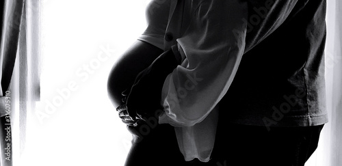 Silhouette of Close up husband's hand hug and touching wife's belly with white curtain background and left copy space in black and white tone. She is pregnant. New life and Lover family concept 