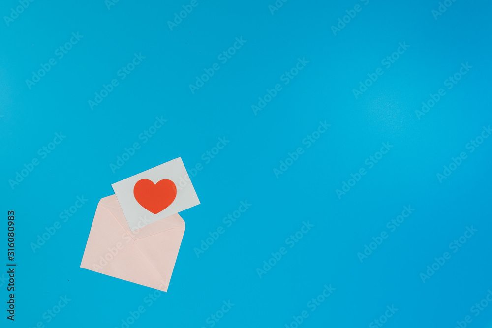Fototapeta premium a red heart on a white paper, on pink envelope, put on the left of the picture on a blue background