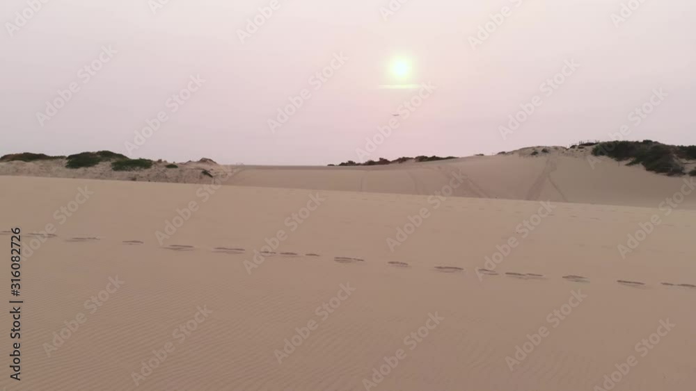 Aerial Drone Follows as Man Runs on Sand Dunes at Red Sunrise near Beach