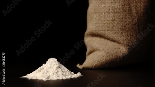 STOP-MOTION: White flour heap growing near a cloth sac on a black background