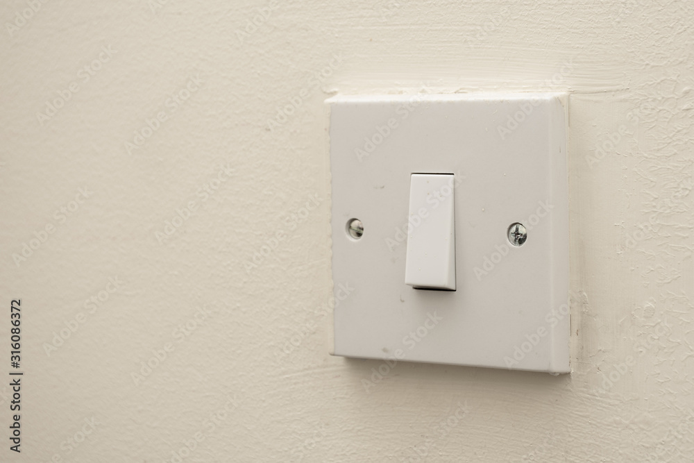 A simple white electrical light switch on a white wall. Industrial, residential or DIY construction concepts. A simple white electrical light switch on a white wall. Industrial, residential or DIY construction concepts.