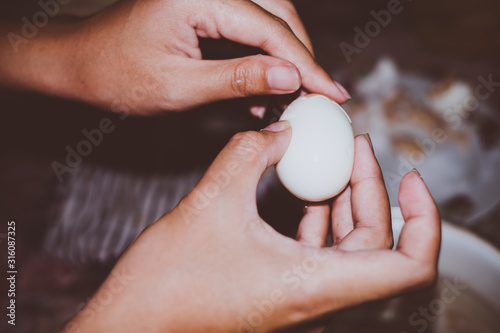 Young lady's hands peeling off shell of boiled egg. Selected focus. Copy space. 