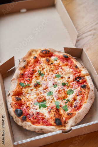 Pizza delivery concept. Baked products in a cardboard box against a wooden background. Baked tasty margherita pizza in Traditional wood oven in Neapolitan restaurant, Italy.