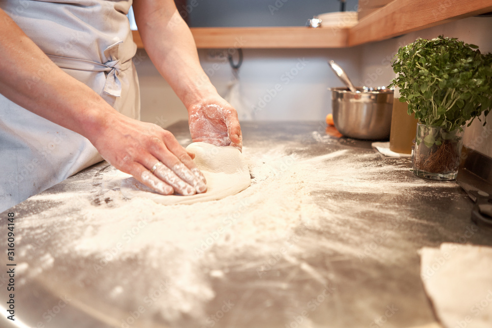 Dough for Neapolitan pizza, the chef rolls out the blanks. Closeup hand of chef baker in uniform white apron cook pizza at kitchen
