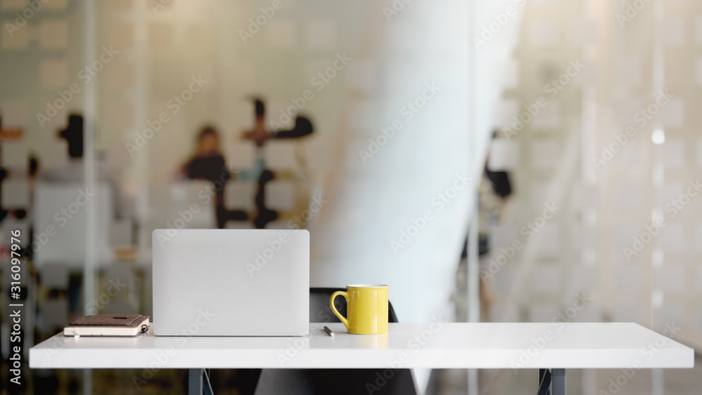 Close up view of workspace with laptop, office supplies, coffee cup and copy space on white table with blurred office room