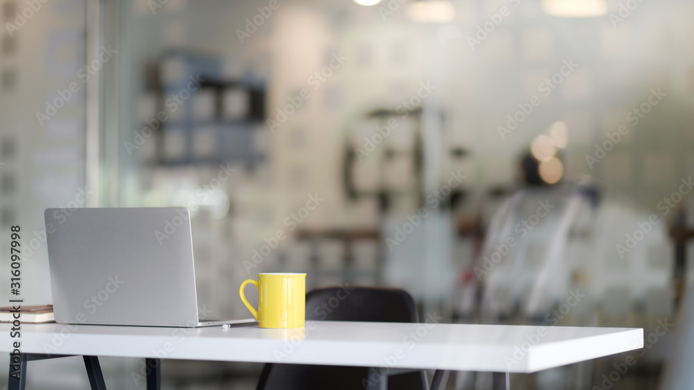 Close up view of workplace with  tablet, office supplies and yellow coffee cup on white table with blurred  office room