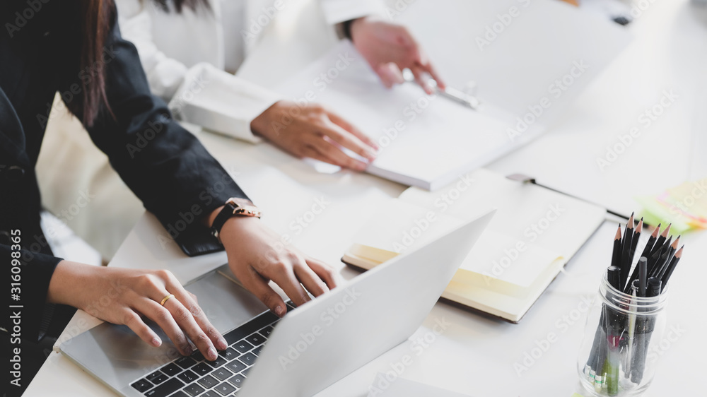 © bongkarn - Close up view of businessman typing on laptop while siting in meeting room with co worker and office supplies