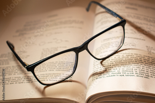 Pair of reading glasses on an opened book, with beautiful shadows falling on the words.