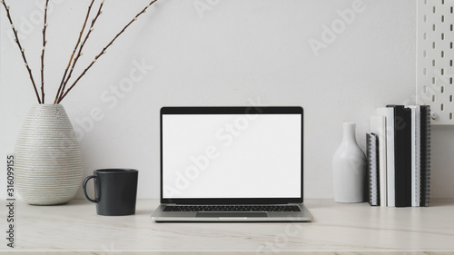 Cropped shot of workplace with blank screen laptop, decorations, books and coffee up on marble desk with white wall