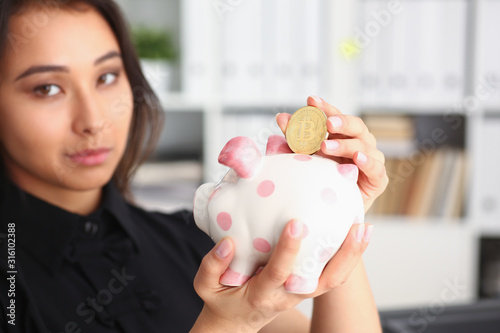 young beautiful brunette woman hold piggybank in arms put money into moneybox photo