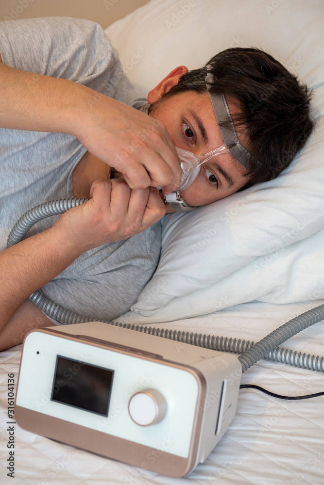 Healthy young man wearing ( CPAP Mask ) nasal mask and using CPAP machine  for sleeping smoothly all