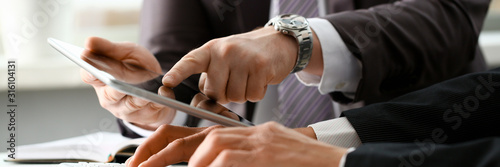 Two businessman are looking and studying statistics on tablet display closeup. Male hand opponent holds pen and points out problem collaboration business coach cooperation partnership palm concept