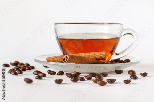 Glass cup of tea with cinnamon sticks and coffee beans. White background. Isolated. Hot spiced cinnamon tea. Close up.