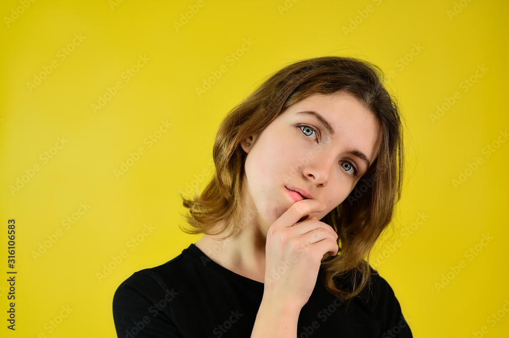 A universal concept, the picture is suitable for any topic. Close-up Studio portrait of a pretty blonde girl in a black T-shirt on a yellow background with bright emotions.