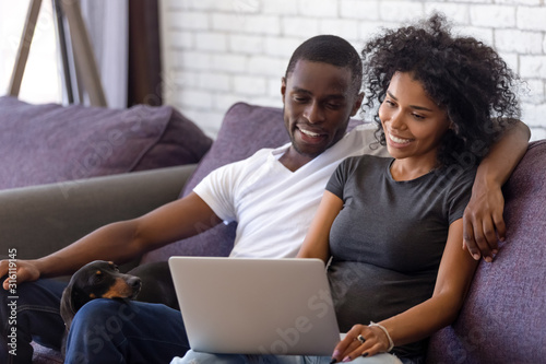 Happy black couple relax with dog watching movie on laptop