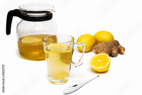 Transparent teapot and mug of herbal tea, lemons, ginger, thermometer on white background. Cold and flu season. Alternative medicine concept. Natural remedies. Copy space