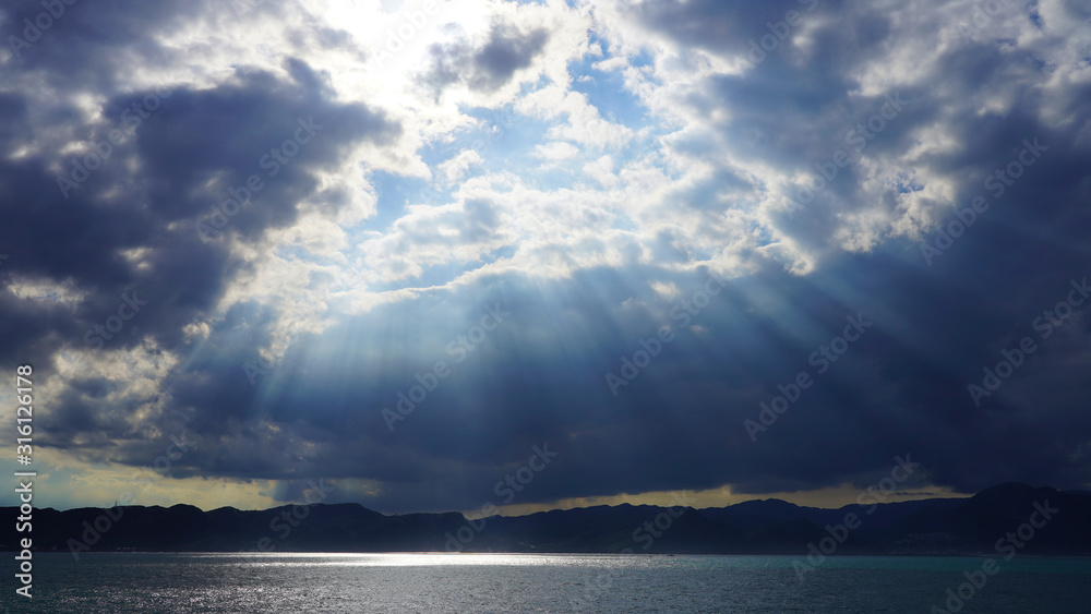 dramatic sky, dark clouds on a blue sky, the rays of the sun pass through the clouds in lines. glow of heaven at sea. ocean