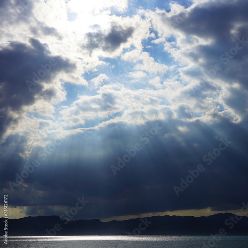 dramatic sky, dark clouds on a blue sky, the rays of the sun pass through the clouds in lines. glow of heaven at sea. ocean © Artem