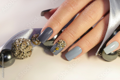 Fashionable grey blue manicure on square shaped nails.Nail art with rhinestones on a light background with decoration.