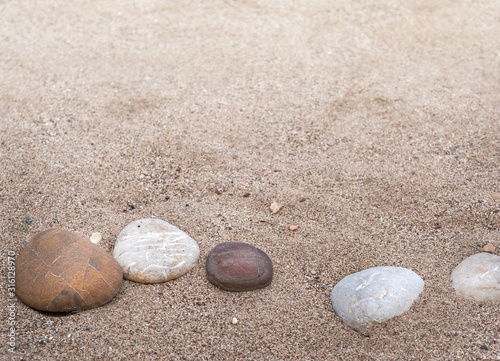 Some sea pebbles in a row of curve line on sandy beach - five stones at soft blur background with copy space for marine concept or decoration in zen style.