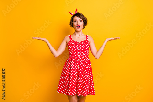 Photo of pretty lady model manager hold open arms product presenting cool novelty two variants wear retro style summer dotted red white dress headband isolated yellow color background photo