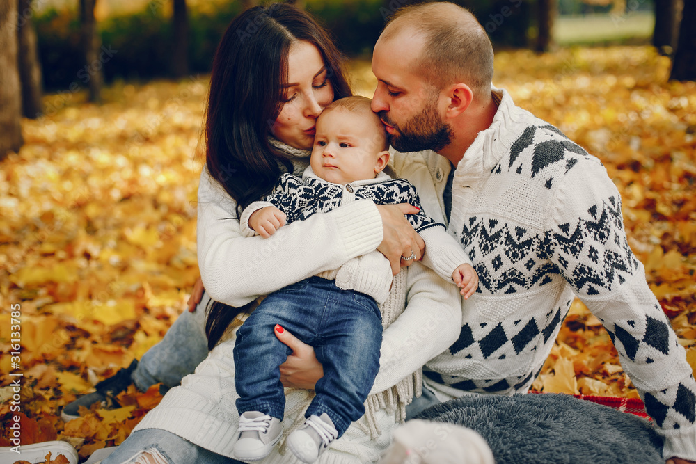 Fototapeta premium Family in a autumn park. Woman in a white sweater. Cute newborn little boy with parents