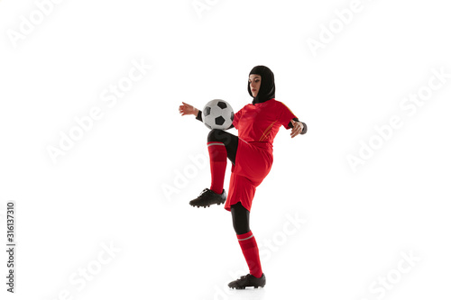Arabian female soccer or football player isolated on white studio background. Young woman kicking the ball  training  practicing in motion and action. Concept of sport  hobby  healthy lifestyle.