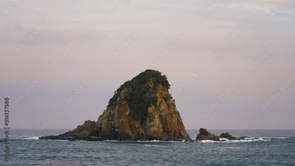 volcanic mountainous islands in the blue water of the Pacific Ocean. tropical islands of Japan overgrown with green plants against a beautiful sunset sky. Aburatsu
